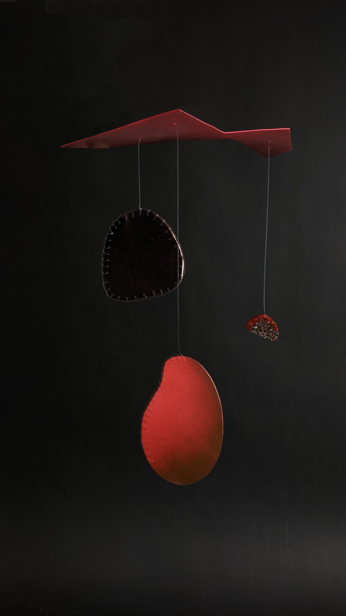 A hanging sculpture  with three pendants, the largest a kidney-bean shape in neon orange/pink with a blanket stitched edge in monofilament. The second larges a rounded trapezoid, likewise edged with blanket stitch monofilament and the final, smallest pendant, made from reclaimed steel shavings and resin.  All suspended from an irregularly shaped aluminium sheet in the same neon orange/pink