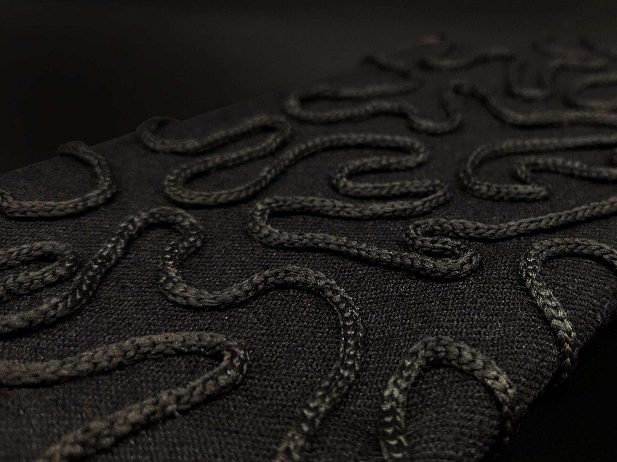 Close up photograph of black couched cord onto black material.